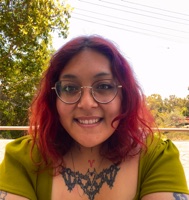 Achi Vasquez smiling outdoors, red hair and glasses
